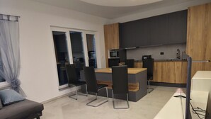 A modern kitchen with wooden cabinets, a dining area with chairs, a sofa, and a TV.