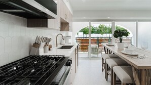Een moderne keuken met een gasfornuis, witte kastjes en uitzicht op een balkon met planten.
