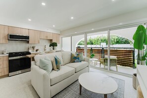 A modern kitchen with a built-in oven and microwave, a beige sofa with decorative pillows, a round dining table, and a large sliding glass door leading to an outdoor area. - The Mizner Pool Suite - Boca Beachside (Boca Raton)