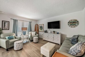 Ein Wohnzimmer mit einer Couch, Hocker, einem Schrank, einem Fernseher und Bildern an der Wand.