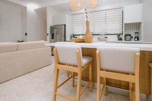 Uma cozinha moderna com armários brancos, uma ilha central com banquetas e um vaso com flores.