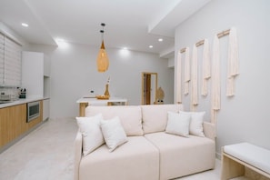 A modern living room with a beige sofa, a dining table, and a kitchen area. - Luxery Apartment | Pool | Playa Flamingo #1 (Brasilito)
