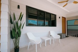 Exterior modern amb una finestra gran, cadires blanques, una planta en test i un ventilador de sostre.