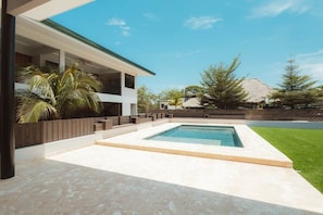 Una casa moderna con piscina, un porche cubierto y un césped cuidado.