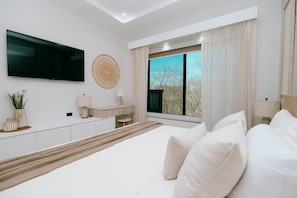 Un dormitorio moderno con una cama grande, un televisor en la pared, un escritorio y una ventana con cortinas.