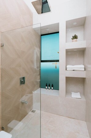 A modern bathroom with a glass shower enclosure, a built-in sink, and a shelf with toiletries. - Luxery Apartment | Pool | Playa Flamingo #1 (Brasilito)