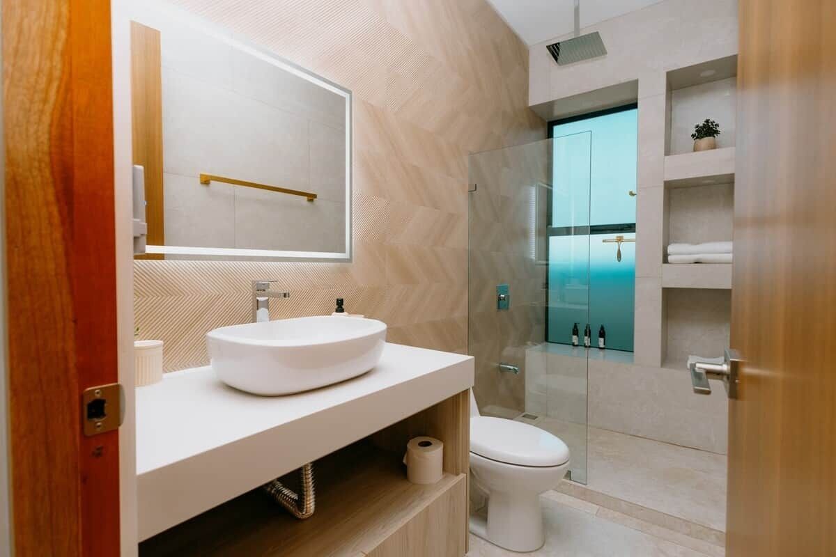 Ein modernes Badezimmer mit einem großen Spiegel, einem runden Waschbecken, einer Toilette und einer Duschkabine aus Glas.