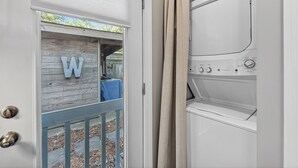 Una puerta con un panel de madera y un letrero con la letra 'W', una lavadora blanca y una cortina color beige.