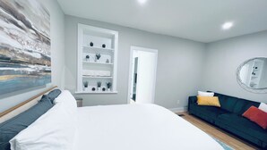 Een slaapkamer met een bed, een inbouwkast met planten, een donkergroene bank, een ronde spiegel en een schilderij aan de muur.