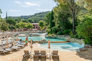 A pool area with lounge chairs and umbrellas, surrounded by greenery and a building in the background. - Ardeche House With Spacious Terrace for 8 (Grospierres)