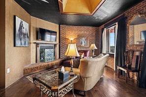 A living room with a fireplace, leather sofa, and a television mounted on the wall. - Upscale, Spacious Apt in the Heart of Downtown. Walk to Restaurants & Breweries! (Hendersonville)