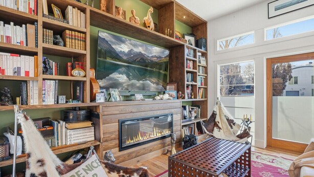 Un salon chaleureux avec une cheminée, des étagères à livres, un grand téléviseur et un tableau représentant un paysage de montagne.