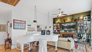 Un salon moderne avec un piano blanc, une cheminée, une bibliothèque et un ventilateur de plafond.