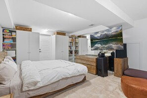 Um quarto com uma cama, uma escrivaninha, uma estante e uma televisão grande.