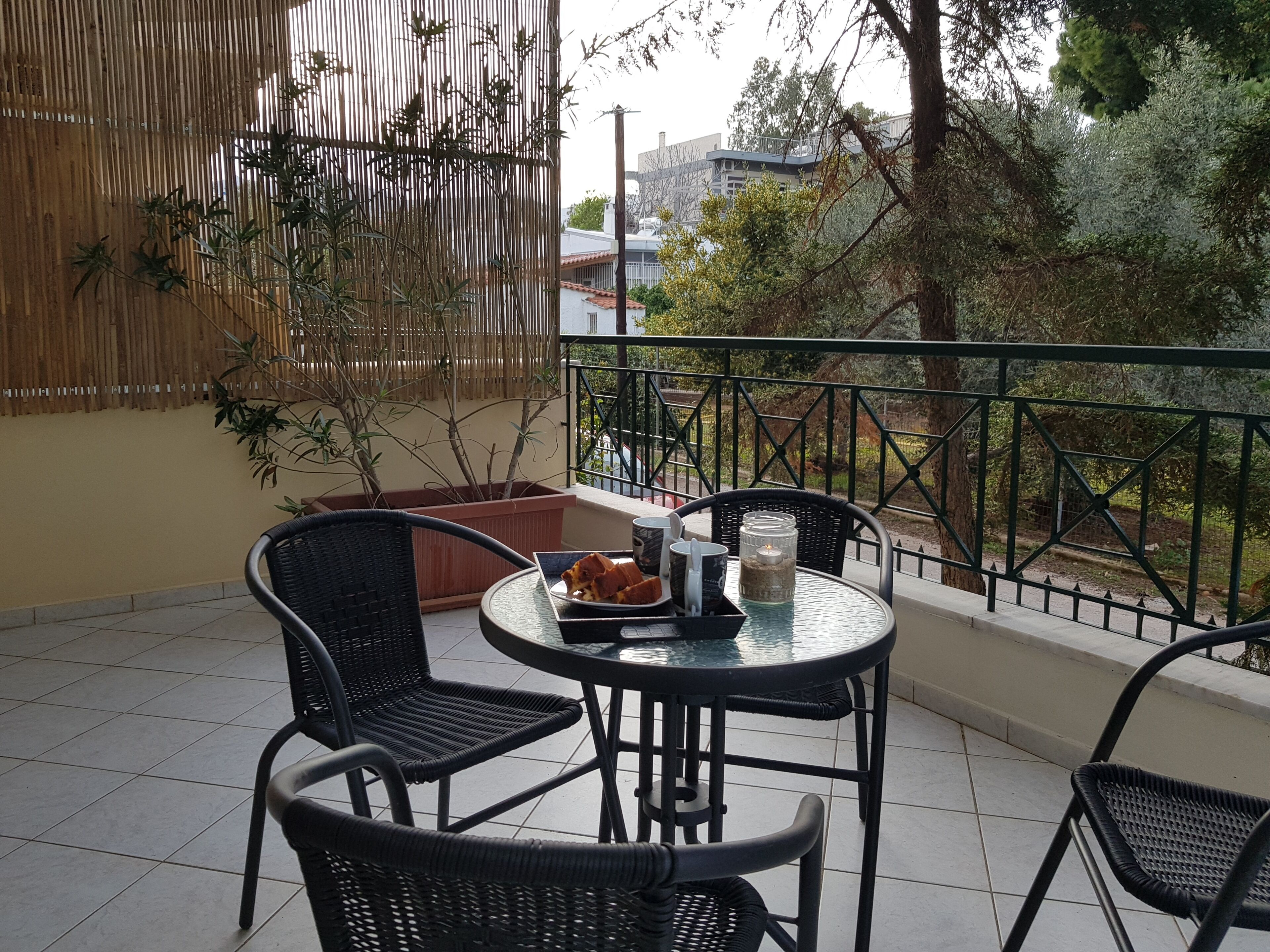 A balcony with wicker chairs, a table, and a potted plant.