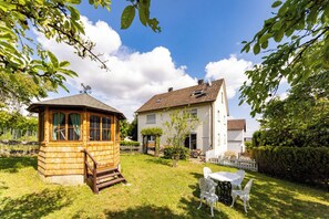 A wooden gazebo, a white house with a tiled roof, and a white table with chairs in a grassy yard. - Apartment Marie (Herbrechtingen)