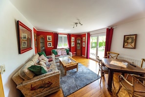 A living room with a sofa, coffee table, and dining table, with red walls and wooden flooring.