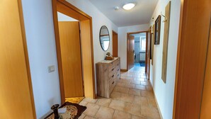 Un pasillo con puertas de madera, un aparador, un espejo y suelo de baldosas.