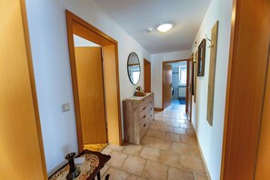 A hallway with wooden doors, a dresser, a mirror, and tiled flooring.