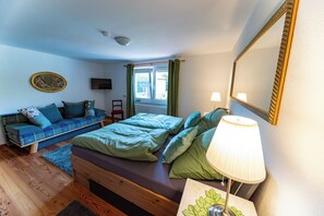 Ein Schlafzimmer mit Bett, Sofa, Lampe, Spiegel und Fenster.