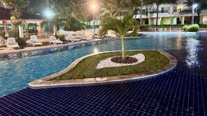 A swimming pool with lounge chairs, palm trees, and a building in the background. - Anchor Flats Condominium by the Sea (Ipojuca)