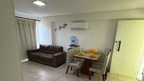 A living room with a sofa, a dining table with chairs, a water dispenser, and an air conditioning unit. - Anchor Flats Condominium by the Sea (Ipojuca)