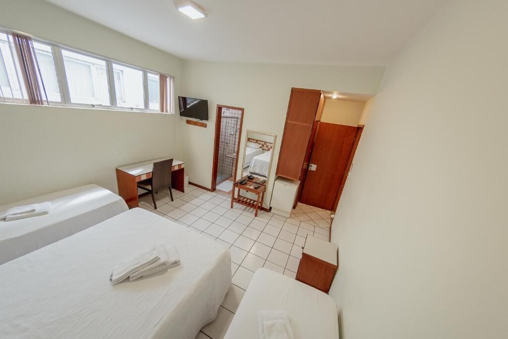 Habitación de hotel con dos camas, un escritorio, un televisor, un armario y baño con espejo e inodoro.