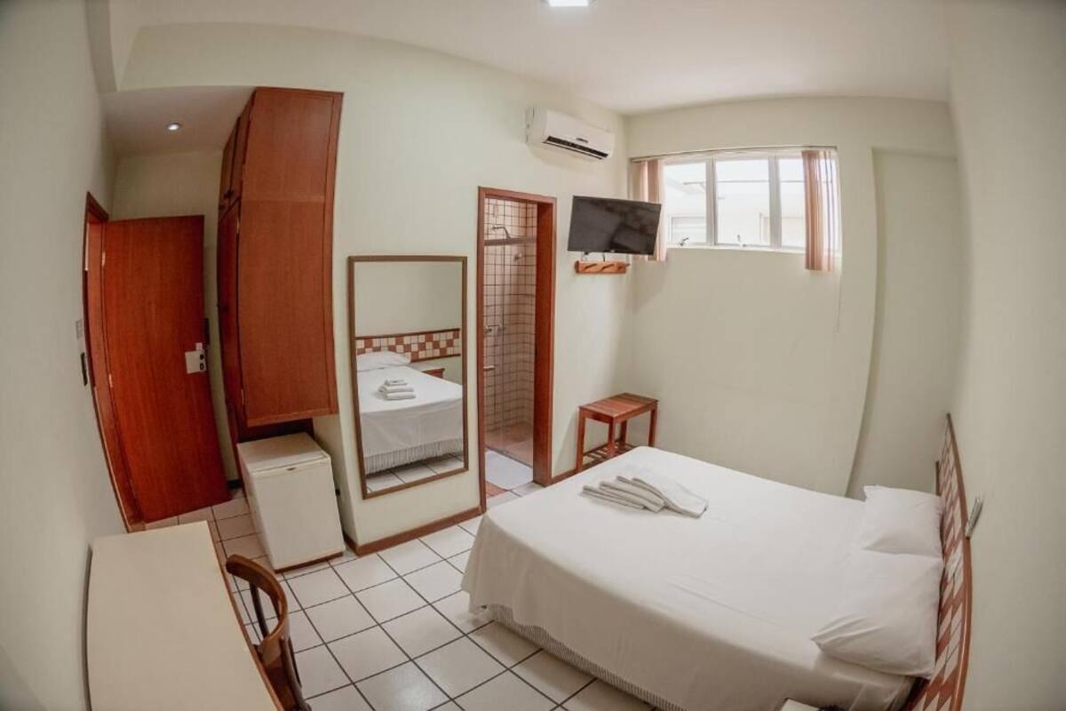A bedroom with a bed, a TV, a small table, a mirror, and a wardrobe.