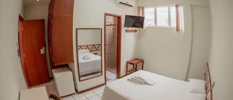A bedroom with a bed, a TV, a small table, a mirror, and a wardrobe.