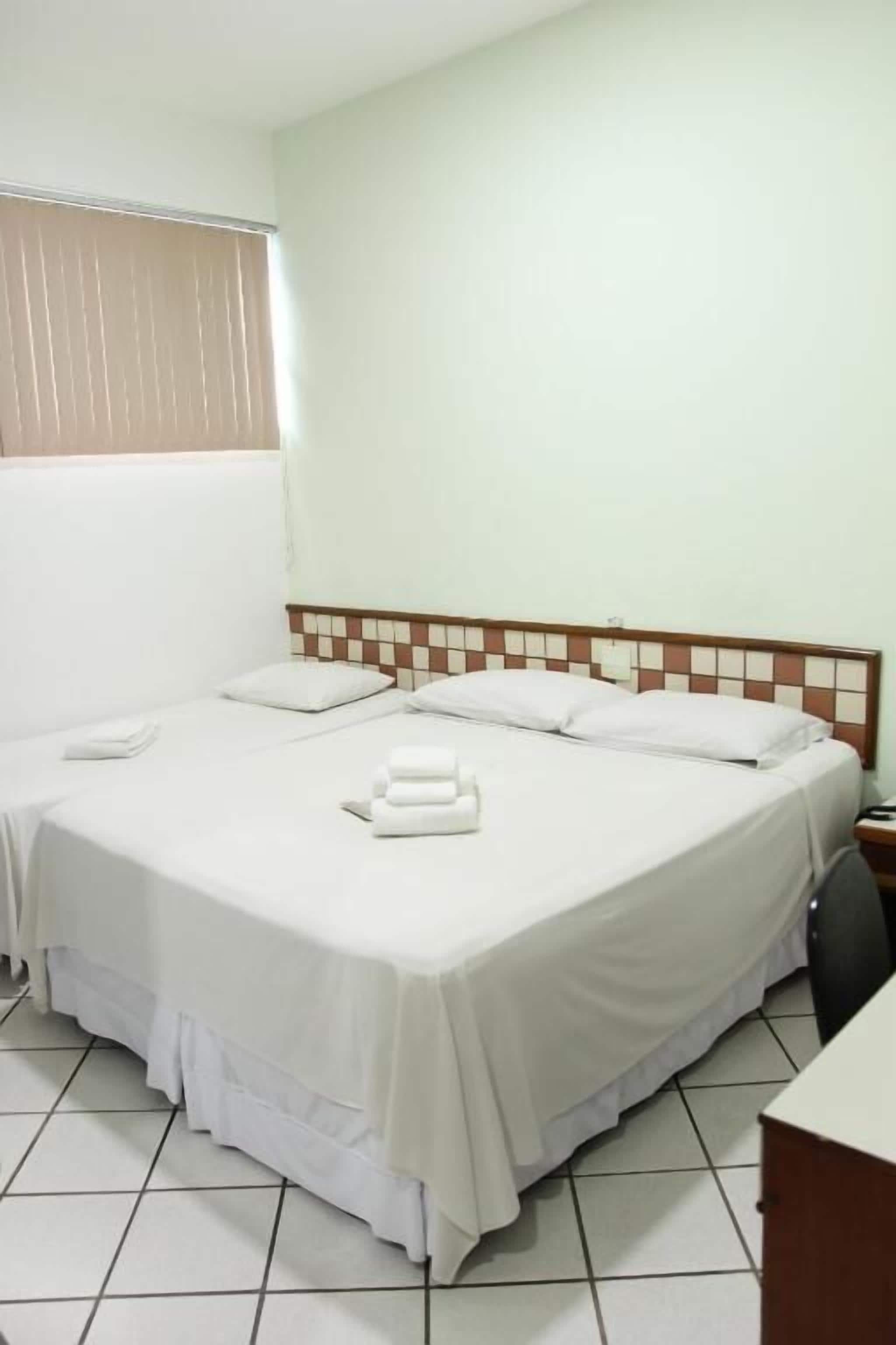 Habitación de hotel con dos camas, suelo de baldosas, ventana con persianas y un diseño de pared a cuadros.