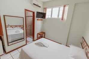 A hotel room with a bed, a television, a window, and a mirror.