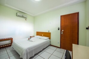 A single-bed room with a wooden headboard, a bedside table, a nightstand, a desk, and a door.