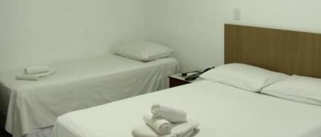 Une chambre d’hôtel avec deux lits, chacun recouvert d’une courtepointe blanche et doté d’oreillers, et une tête de lit en bois.