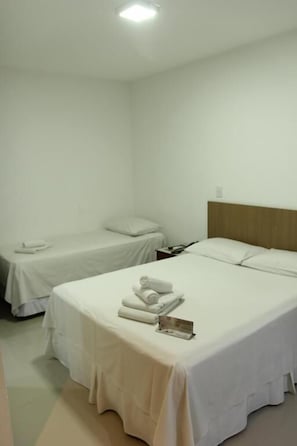 Une chambre dâhĂŽtel avec deux lits, chacun recouvert dâune courtepointe blanche et dotĂ© dâoreillers, et une tĂȘte de lit en bois.