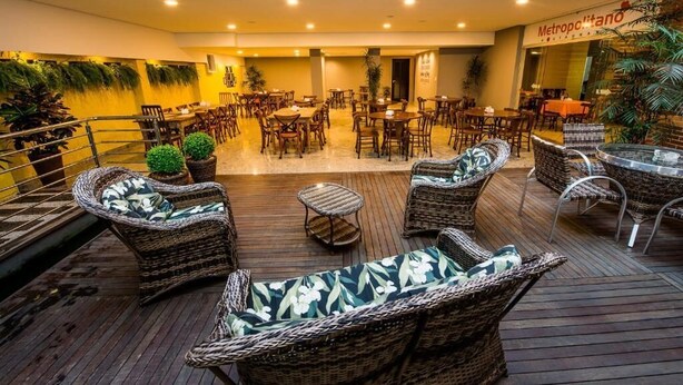 An indoor dining area with wicker furniture, a wooden deck, and a sign reading 'Metropolitano Restaurante'. - Hotel Metropolitano (Coronel Fabriciano)