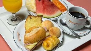 A tray with food items including bread, a sandwich, croissants, watermelon, and a cup of coffee. - Hotel Metropolitano (Coronel Fabriciano)