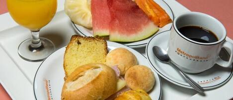 Un vassoio con generi alimentari tra cui pane, un panino, croissant, anguria e una tazza di caffè.