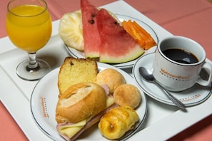 A tray with food items including bread, a sandwich, croissants, watermelon, and a cup of coffee.