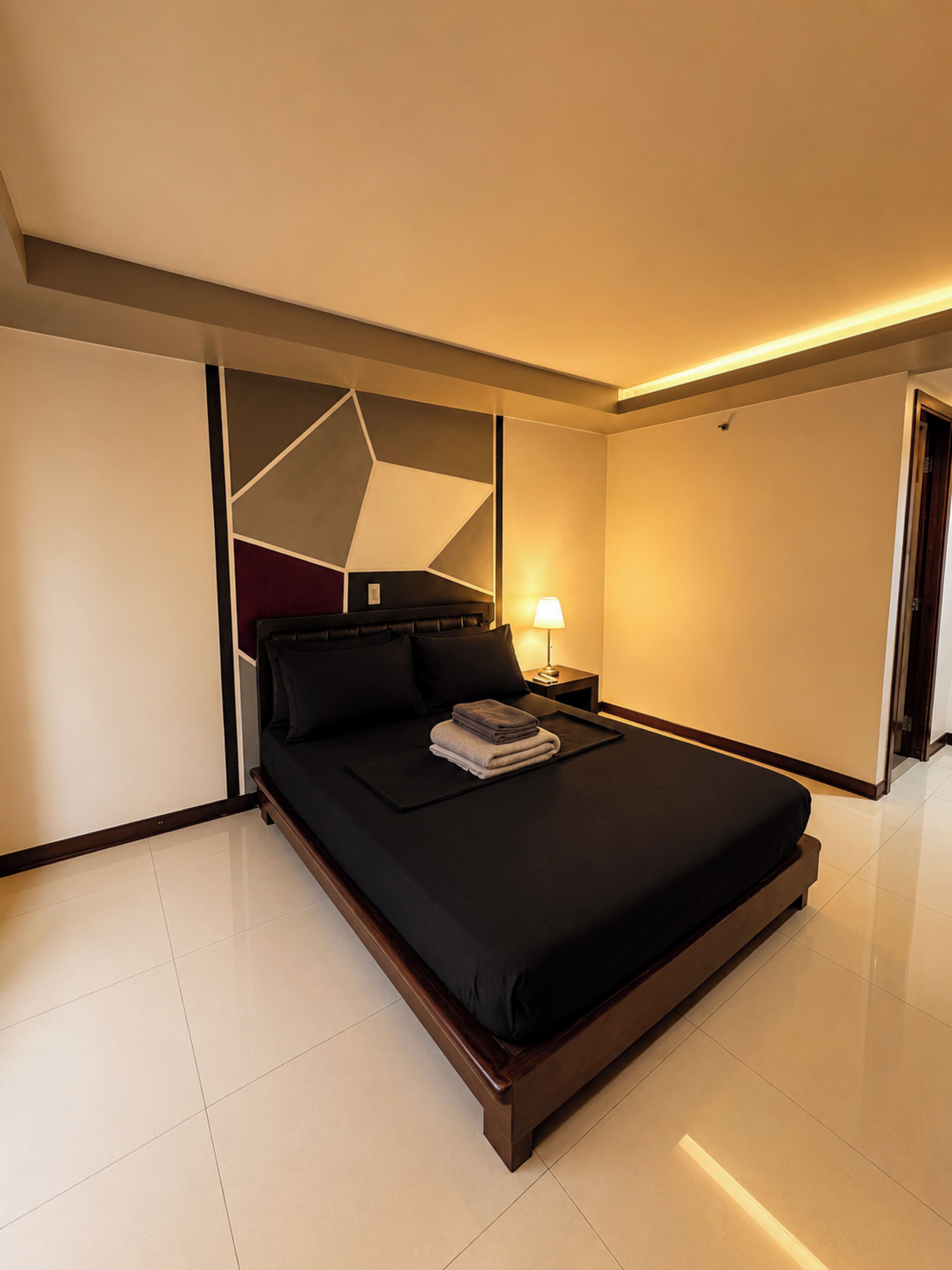 A modern hotel room with a large bed, a bedside table with a lamp, and a geometric wall design.