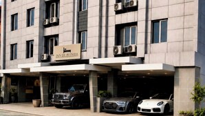 Un hotel de varios pisos con un diseño moderno, que cuenta con unidades de aire acondicionado, un estacionamiento y un letrero que indica el nombre 'Inn de Avenida'.