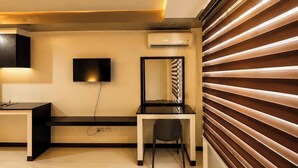 Un dormitorio moderno con una cama, un escritorio, una silla, un televisor y un equipo de aire acondicionado.