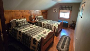Ein Schlafzimmer mit zwei Betten, einem Fenster, einem Deckenventilator und einem Holzboden.