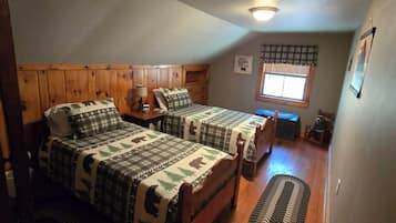 Une chambre avec deux lits, une fenêtre, un ventilateur de plafond et un plancher en bois.