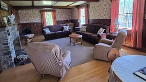Ein geräumiges Wohnzimmer mit Holzböden, einem Kamin und einer Steinwand. Es gibt mehrere Sitzbereiche mit Sofas und Sesseln.