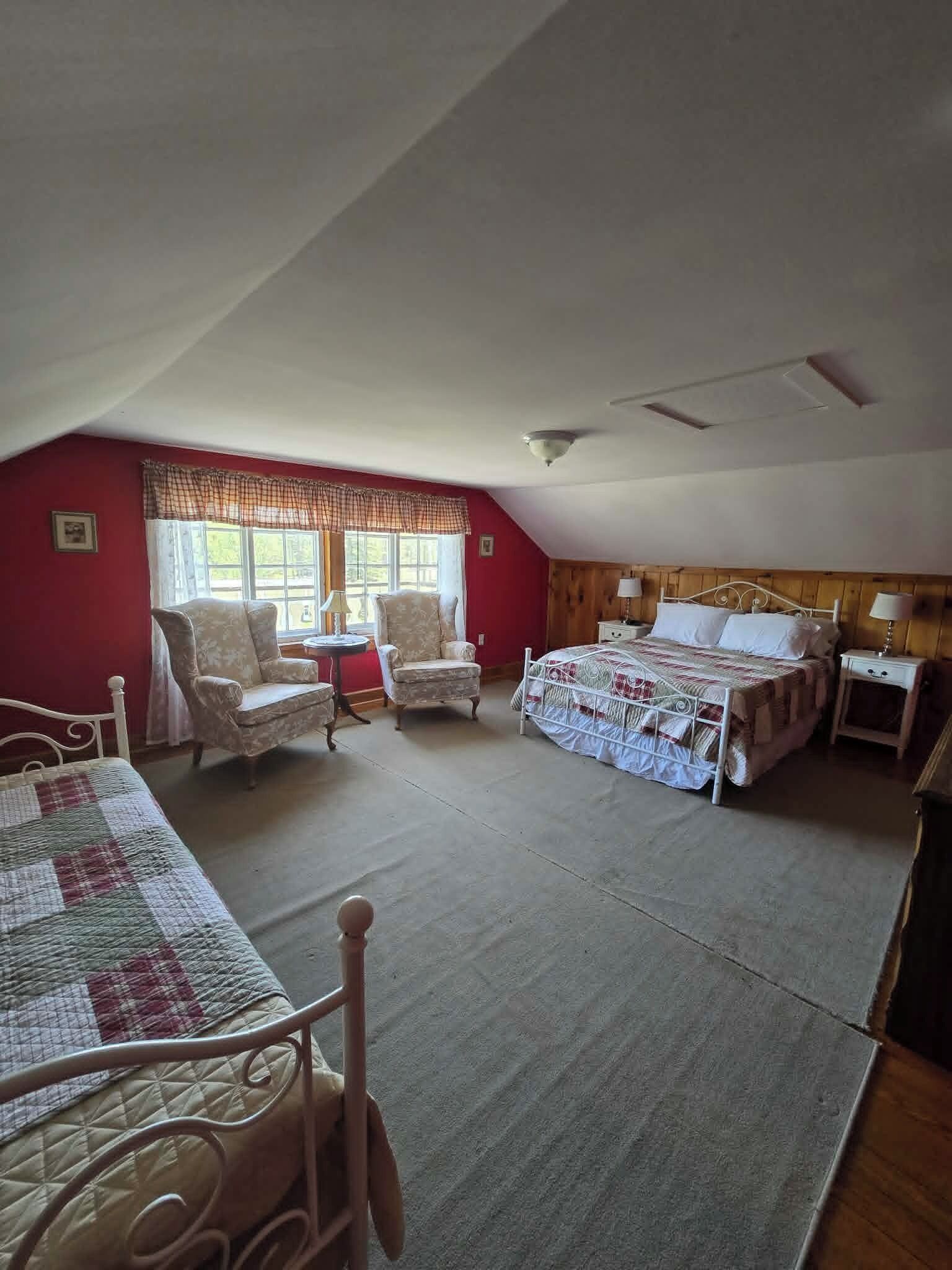 A bedroom with a bed, two chairs, a small table, and a window with curtains.