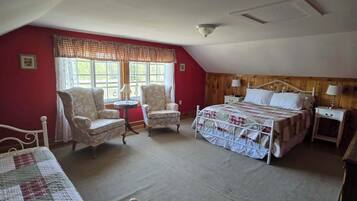 A bedroom with a bed, two chairs, a small table, and a window with curtains.
