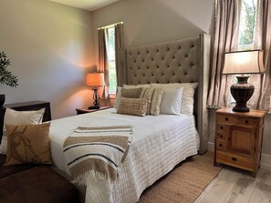 Een slaapkamer met een groot bed, een nachtkastje met een lamp, een houten kast en een raam met gordijnen.