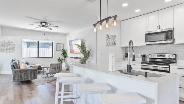 Une cuisine moderne avec des meubles blancs, un îlot central doté de tabourets, un ventilateur de plafond et une grande fenêtre.