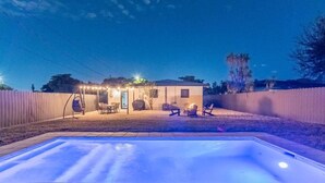 Un jardin avec une piscine, un espace barbecue et une maison dotée d’un porche.
