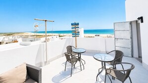 En takterrass med två runda bord och stolar, en skylt som visar vägen och utsikt över stranden.